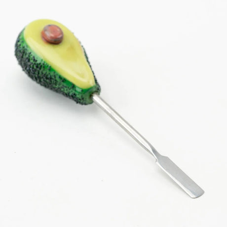 Avocado glass dabber lying on white surface, focus on wide stainless blade and lifelike pit in yellow fruit body.