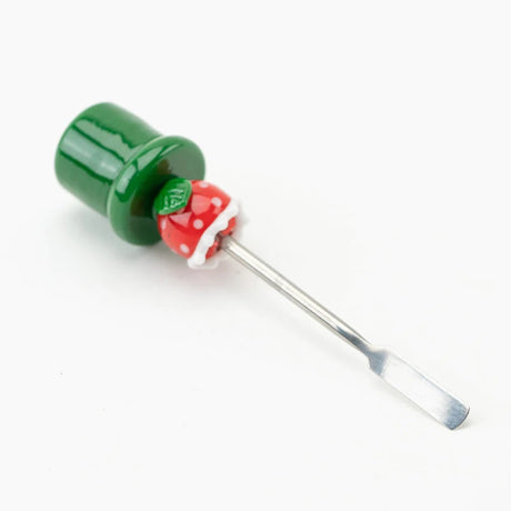 Angled shot of piranha-plant glass dabber lying down, focusing on stainless blade and weighted green base on white surface.