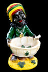 Standing Rasta figurine resin ashtray holding cream bowl with leaf decor, vibrant green shirt and woven cap, black backdrop.