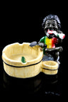 Resin ashtray with seated Rasta in tie-dye shirt beside rustic bucket-style bowl and extra cup holder, glossy black stage.
