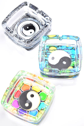 Square glass ashtray trio with yin yang art in clear, rainbow, and mosaic looks, top-down studio shot.