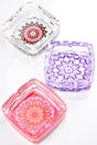 Square glass ashtray trio displaying pastel mandala patterns in aqua, lavender, and coral hues, overhead view.