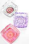 Square glass ashtray trio displaying pastel mandala patterns in aqua, lavender, and coral hues, overhead view.