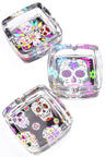 Square glass ashtray trio showing colorful sugar skull motifs on black base, bright pop-art presentation.