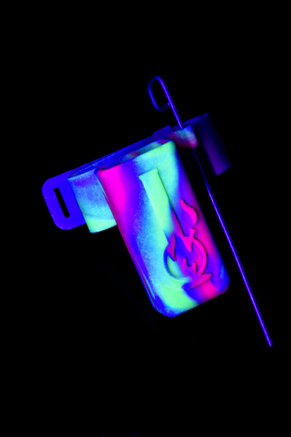 Neon swirl silicone water pipe caddy glowing under blacklight with attached metal poker tool on a dark background.