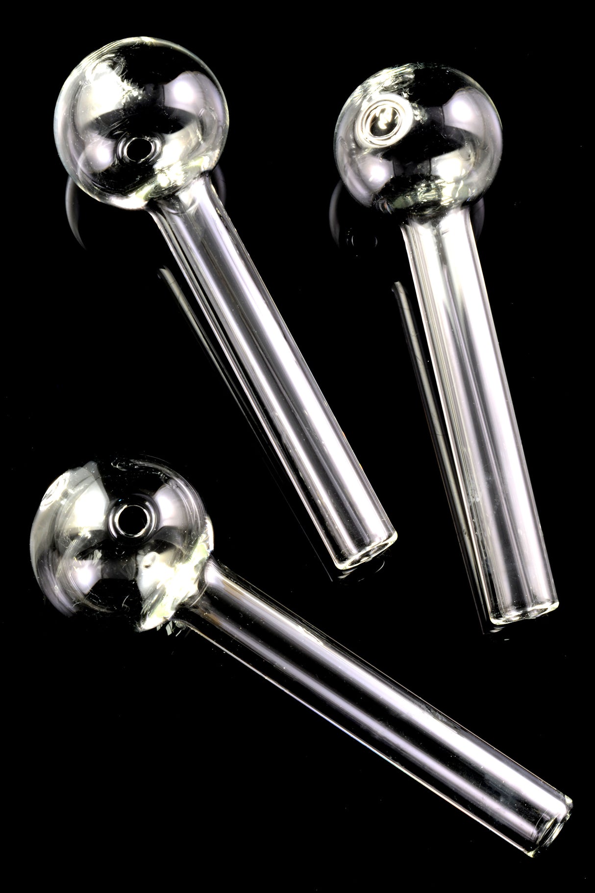 Cluster of three 4-inch clear thick-walled glass oil burner pipes on glossy black surface, showcasing round bowl ends