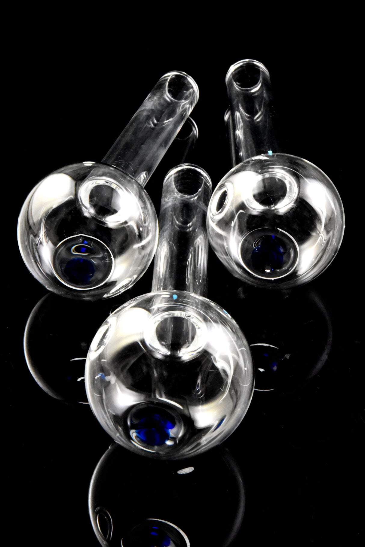 Close-up of three thick glass oil burner pipe bowls with blue dot accents, viewed from above on glossy black background.