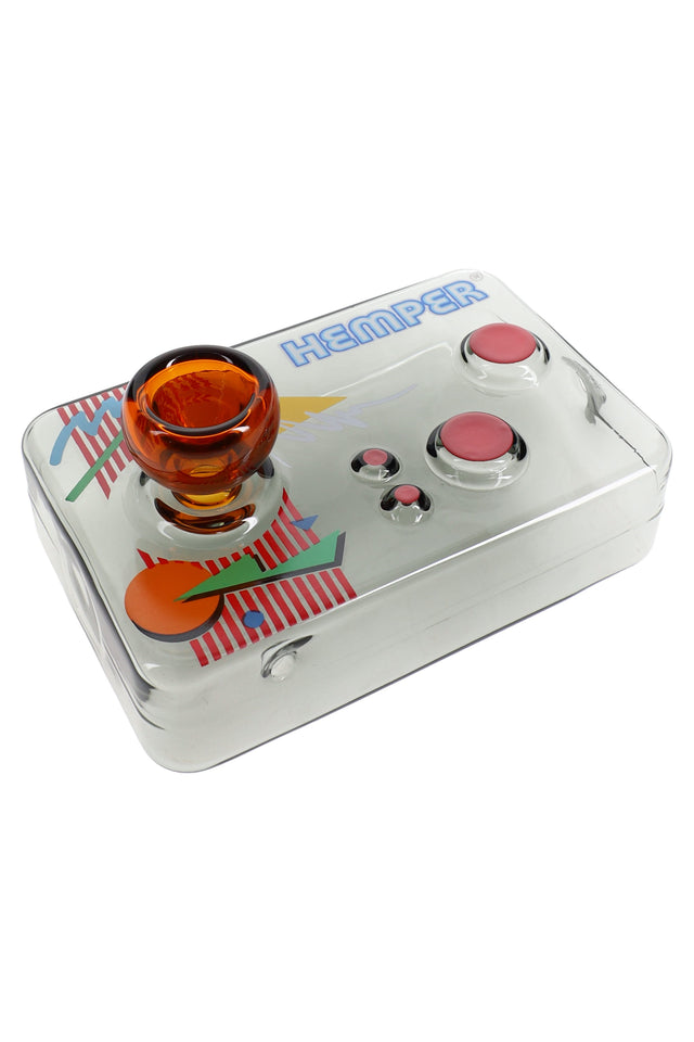 Transparent black arcade controller glass hand pipe with amber joystick bowl and pink-red buttons resting on a white studio background.