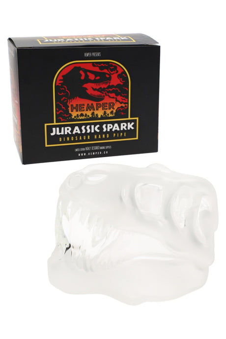 Hemper Jurassic Spark T-Rex skull glass hand pipe posed in front of matching black and red dinosaur retail box on white backdrop.