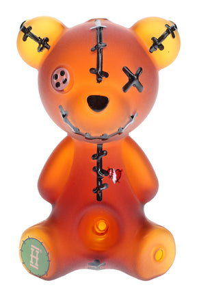 Frosted amber Hemper Scare Bears teddy bear glass hand pipe with black stitches and heart graphic standing upright on white.