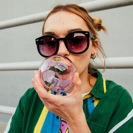 Person holding Goody Glass Peachy hand pipe with round pink body and green stem detail