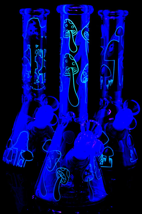 Trio of glow mushroom beaker bongs under UV light highlighting neon outlines; ice pinch and glass-on-glass joints visible, assorted graphics.