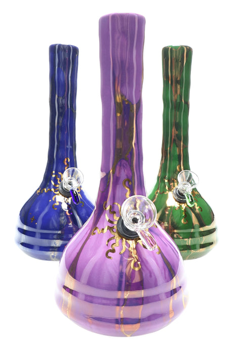 Hand-thrown 9-inch ceramic beaker water pipe with 22 k gold sunburst design, shown in purple, blue, and green glazes with glass slide and grommet bowl on white background.