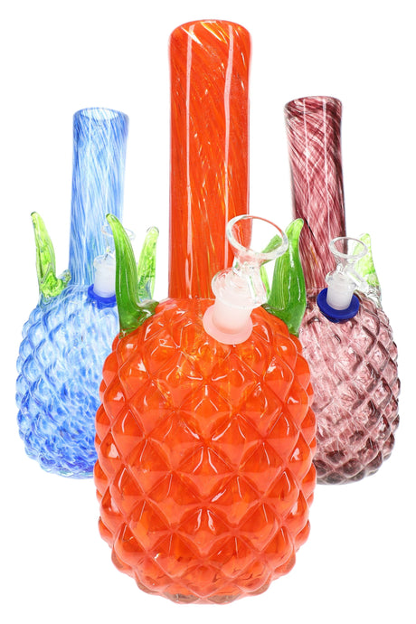 Close trio of pineapple-textured soft glass bongs showing orange, blue, and rose colorways with green leaf accents and swirled necks.