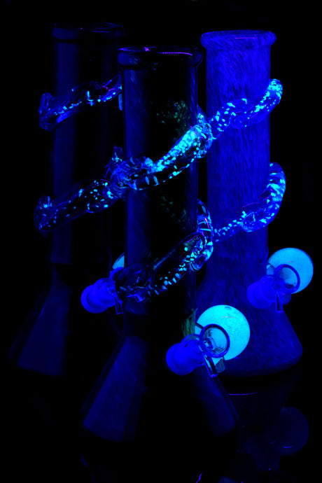 UV-reactive soft glass beaker bongs glowing under blacklight; spiral neck rings and marbles illuminate for night sessions.