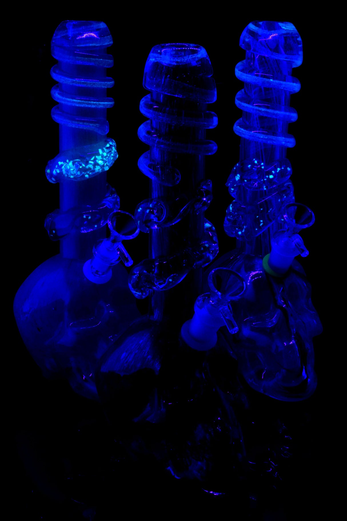 UV-reactive soft glass skull bongs glowing under blacklight; select spiral rings illuminate for nighttime sessions and display.