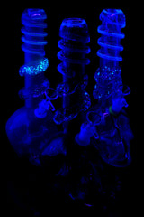 UV-reactive soft glass skull bongs glowing under blacklight; select spiral rings illuminate for nighttime sessions and display.
