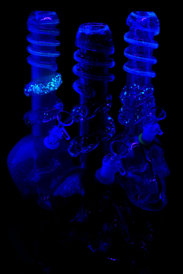 UV-reactive soft glass skull bongs glowing under blacklight; select spiral rings illuminate for nighttime sessions and display.