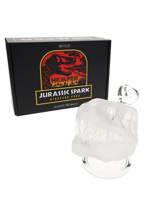 Hemper Jurassic Spark dinosaur skull bong displayed in front of black and red branded box, three-quarter view highlighting frosted glass design.
