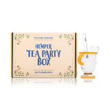 Wide shot of Hemper Tea Party Box next to tea cup glass bong, white cup body with amber accents and bowl