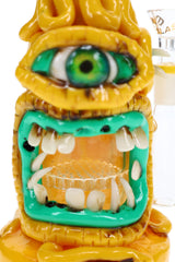 Close-up of cyclops bong with green eye, sculpted teeth, and honeycomb perc visible through the open mouth.