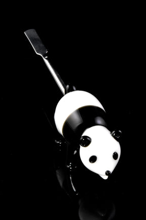 Glass panda dab tool with stainless-steel flat scoop tip, standing on glossy black surface for dramatic contrast, front three-quarter view.