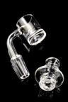 Close view of clear quartz spinner banger and turbine carb cap on black background; two beads inside bucket.