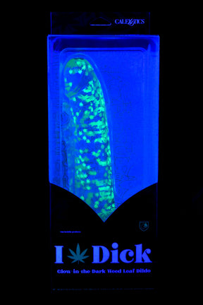 Naughty Bits “I Dick” glow-in-the-dark weed leaf dildo glowing under black light with curved shaft and suction-cup base in retail packaging.