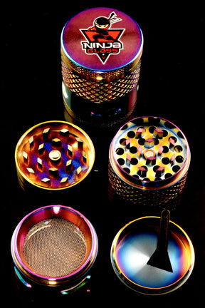 Close-up of Ninja Glass rainbow windowed metal herb grinder parts on black background, mesh screen and kief tray visible.