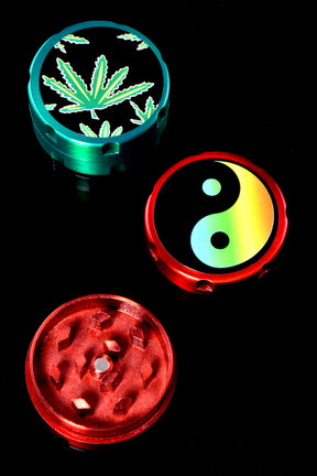 Mini 2-piece metal herb grinder with rainbow yin-yang lid and red body on black background, disassembled view.