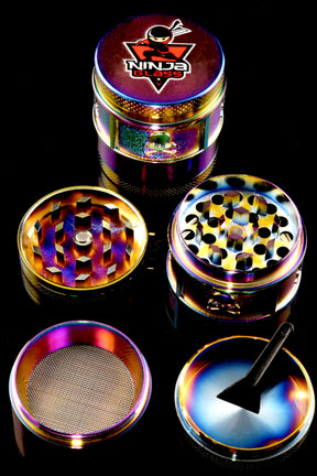 Close-up of Ninja Glass rainbow 4-part metal grinder on black background with diamond teeth, fine mesh screen, and kief tray visible.