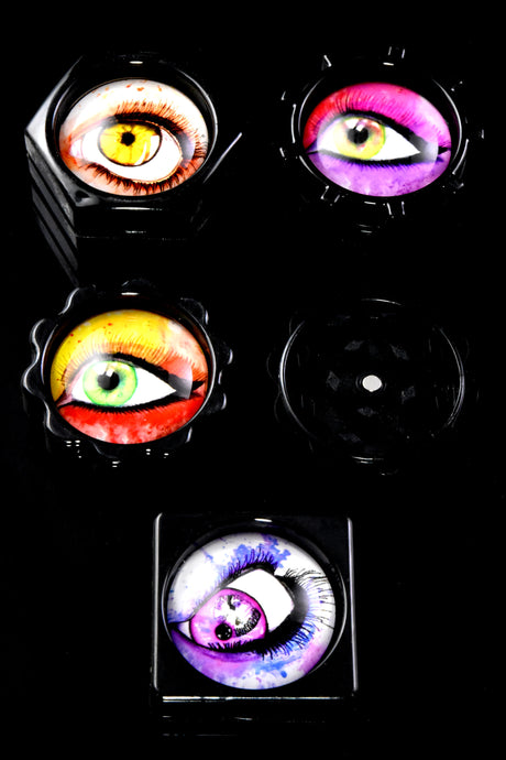 Close-up of four plastic eyeball herb grinders on black background, assorted shapes, two-part design with magnet and textured grip.