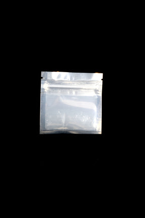 Silver-backed, clear-front Mylar zip bag, 3 × 3 inches, lying flat on black background, showing zipper and tear-notch top opening